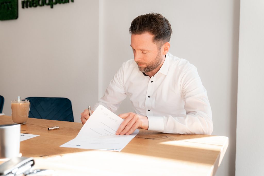 Tammo Horn, Geschäftsführer von Medoplan, unterschreibt Managementverträge am Schreibtisch.