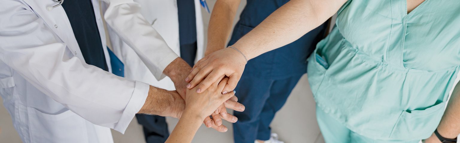 &Auml;rztinnen, &Auml;rzte und Praxisteam legen die H&auml;nde &uuml;bereinander